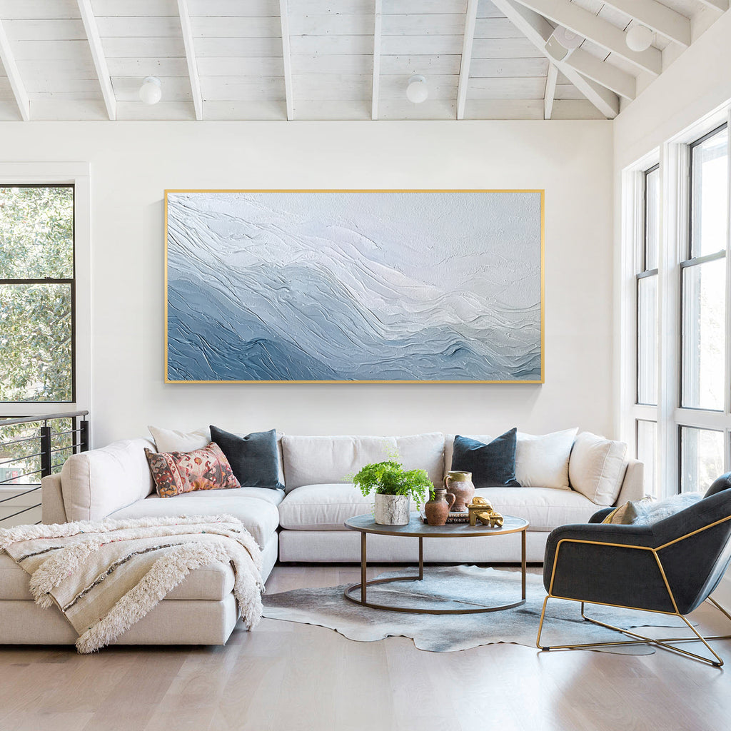Blue and white textured abstract wall art painting displayed above a sofa in a bright modern living room