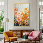 Colorful floral wall art with pink, orange and yellow flowers in a gold frame above accent chairs in a modern living room