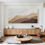 Modern abstract textured wall art with light wood frame displayed above a wooden cabinet in a minimalist living room, neutral beige and brown canvas artwork for home decor
