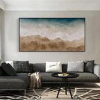 Textured ocean wave and beach wall art with black frame above a sectional sofa in a modern living room